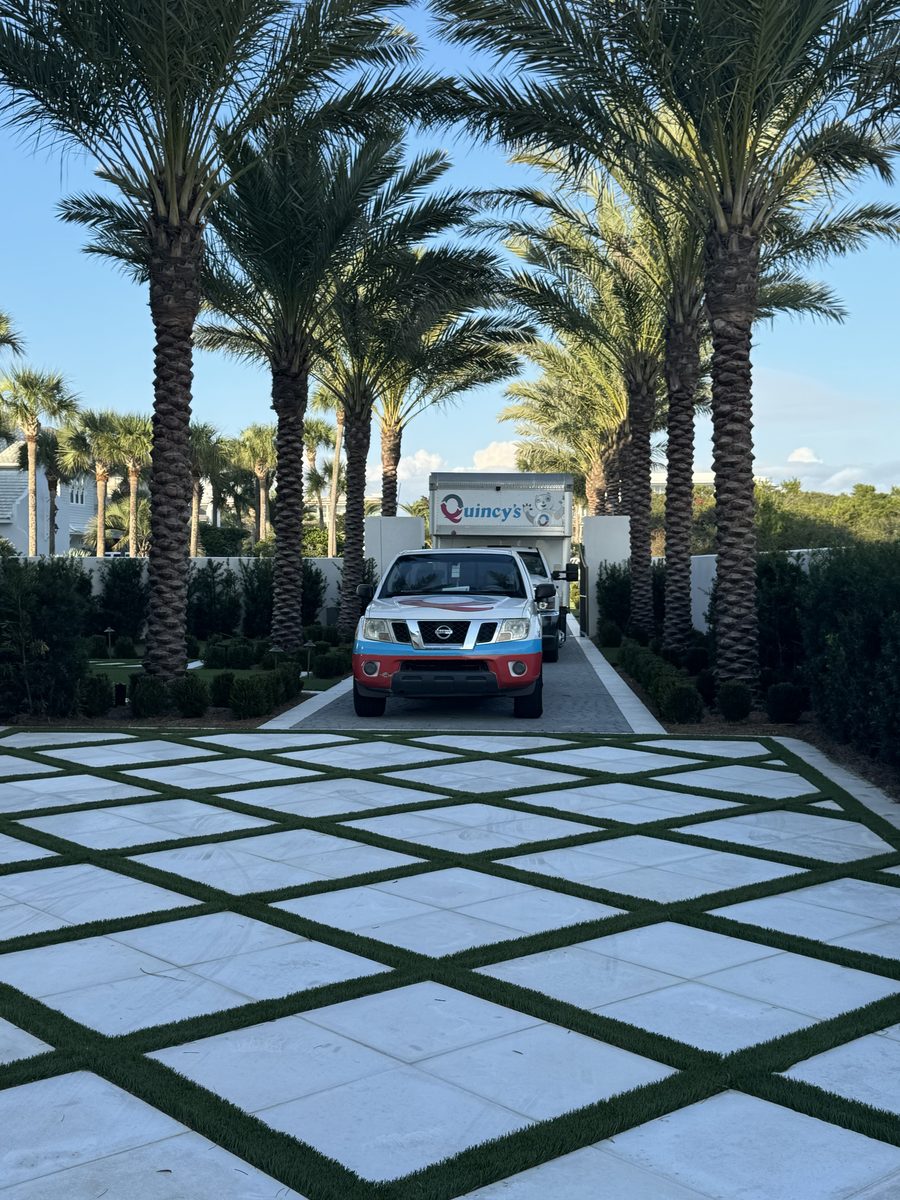 Quincy's branded pickup truck and service box truck arriving at a luxury Emerald Coast home lined with tall palms