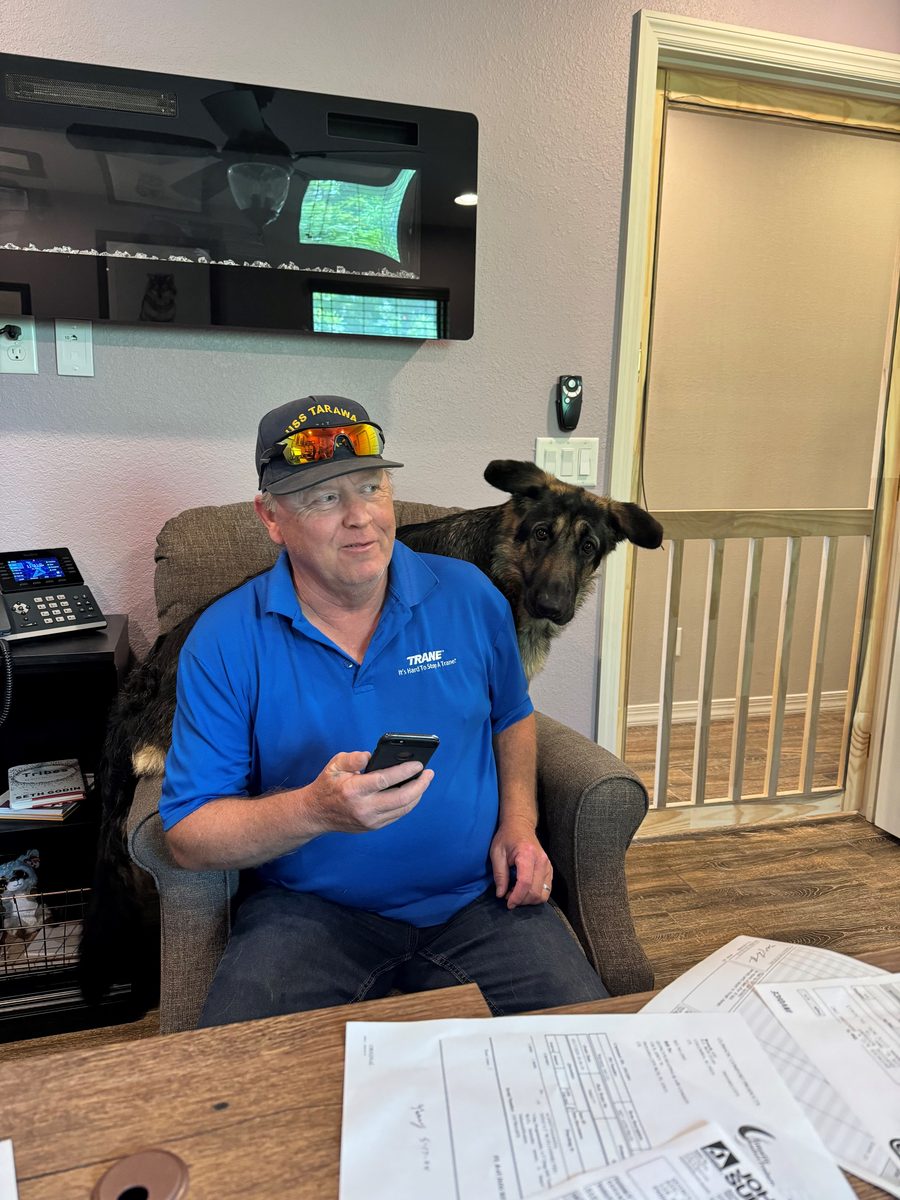 Keith Walker in his Trane shirt at the Quincy's office desk, a German Shepherd leaning over his shoulder from behind