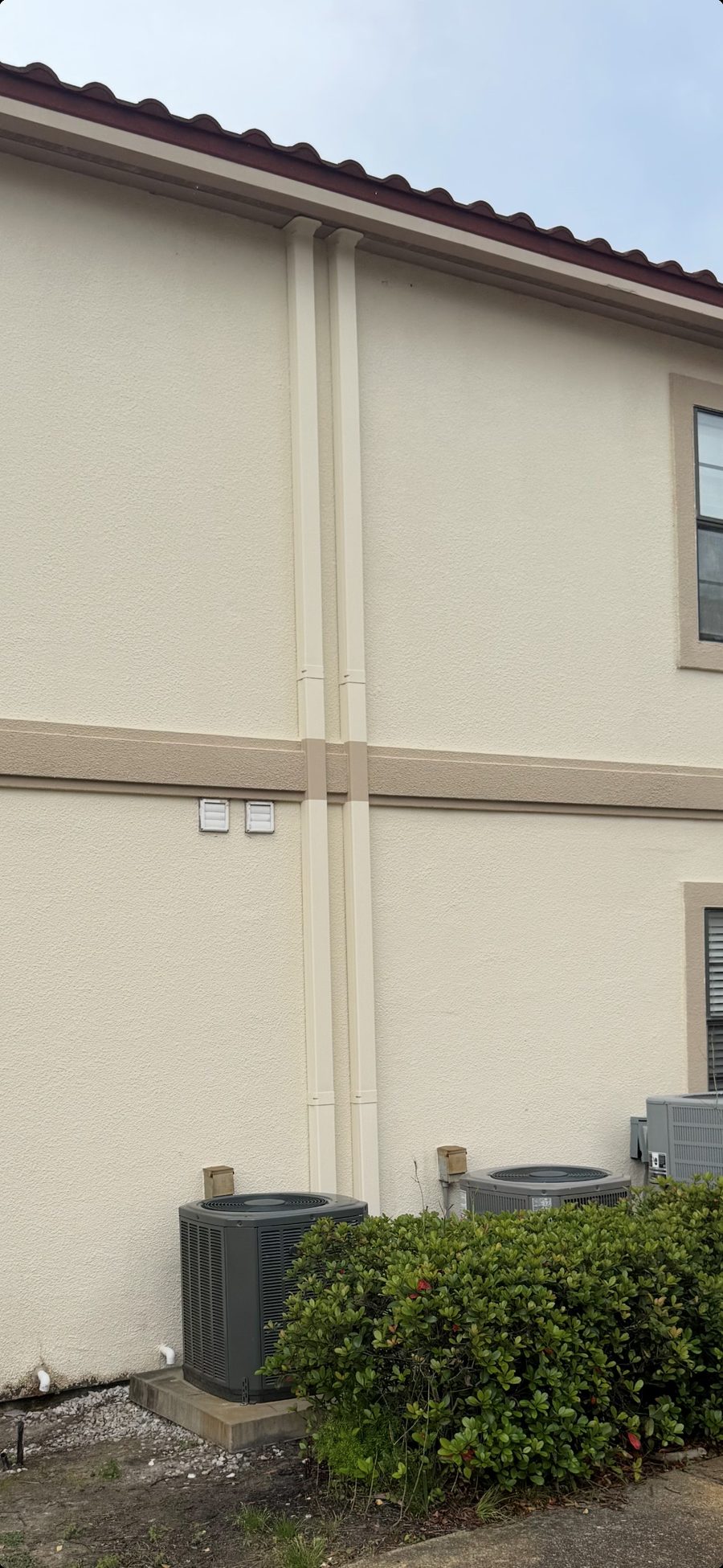 Clean matching lineset covers running up a stucco building exterior, two outdoor AC condensing units installed below