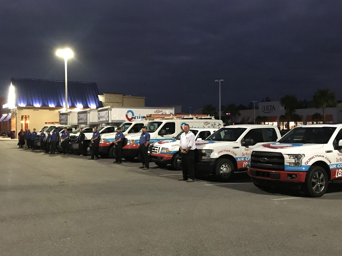 Quincy's Heating & Air full team standing beside their entire branded fleet of service trucks at night — Panama City Beach, FL