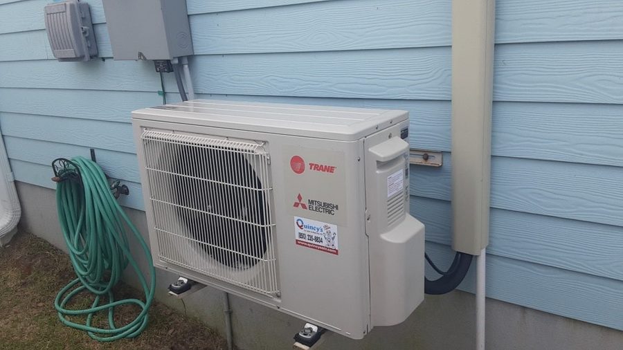 Trane Mitsubishi Electric outdoor unit installed cleanly on a blue coastal home with Quincy's service sticker visible